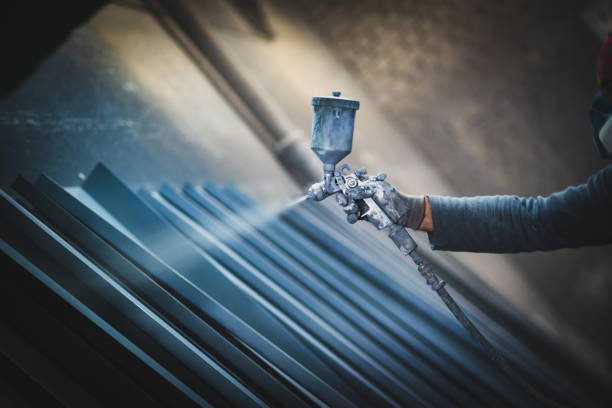 man painting metal products with a spray gun.